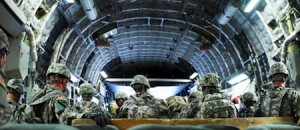 U.S. infantry troops disembark from a C-17 military freight aircraft in Baghdad’s international airport. After leaving the aircraft to travel in an armored bus, soldiers were warned about the danger of flying glass shards caused by an IED.