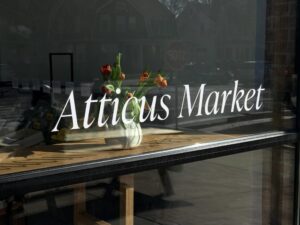 An up close view of the wordmark of Atticus Market on its window.
